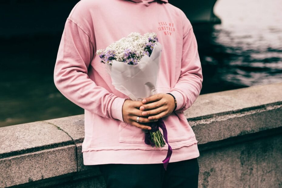 a man wearing a pink hoodie and holding a bunch of flowers, waiting for his date